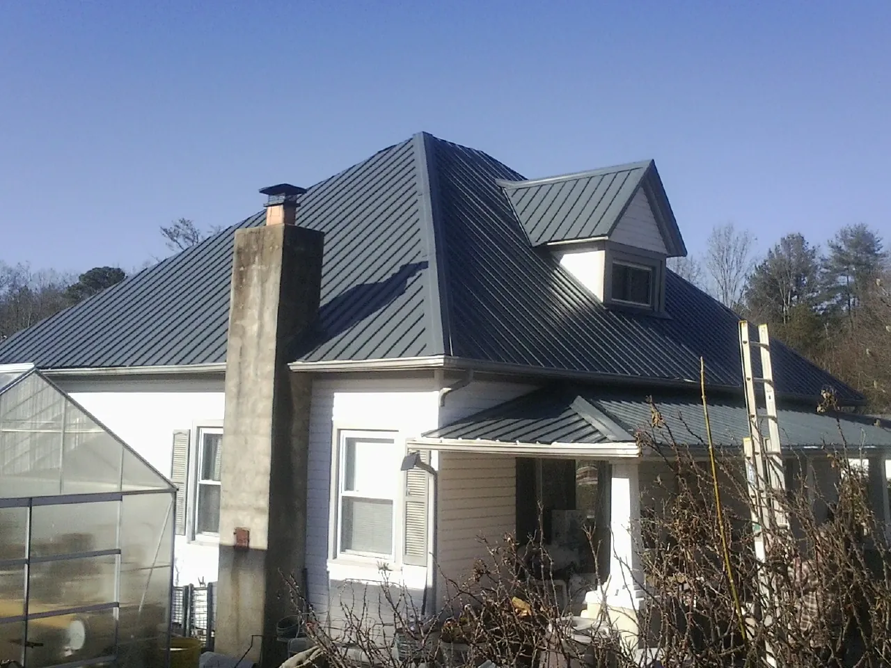 Dark blue standing seam metal roof on a white farmhouse with dormer — Slate & Tile Roof Repair by Roofing Brothers in Apison