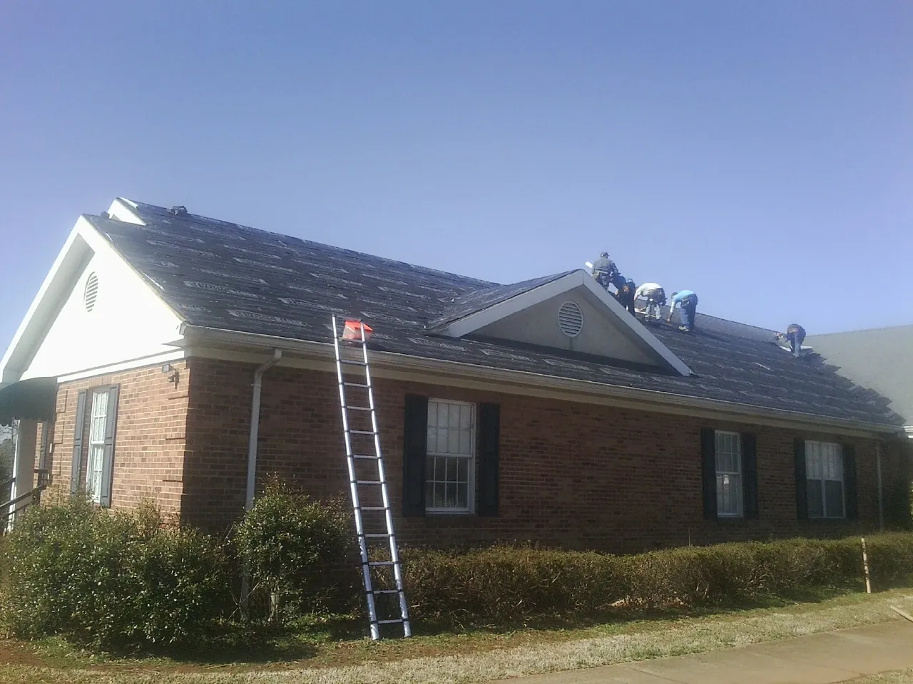 Crew tearing shingles off a brick ranch roof with a ladder set — Emergency Roof Repair work by our crew in Apison