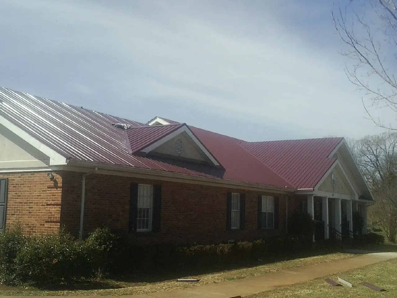 Red metal roof with gabled entries on a long brick building, from a Hail Damage Roof Repair job in Apison