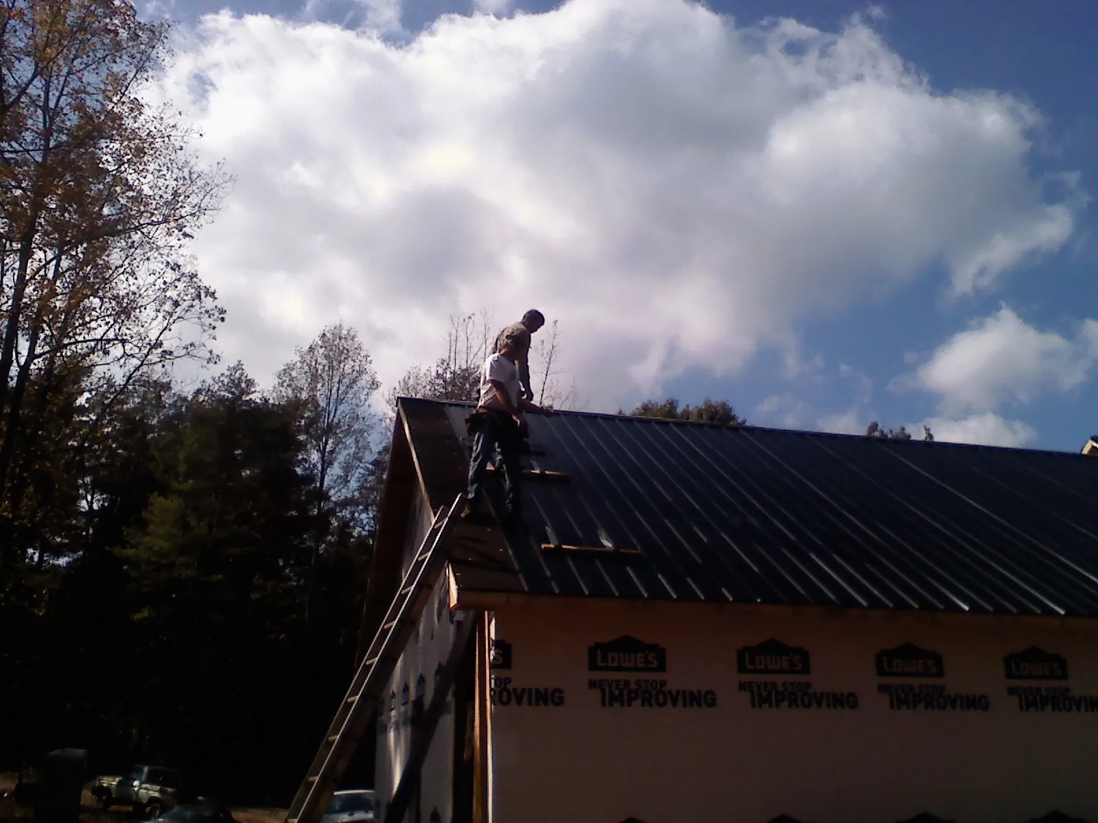 Roofer fastening dark metal panels high against a cloudy sky, from a Roof Inspection job in Apison